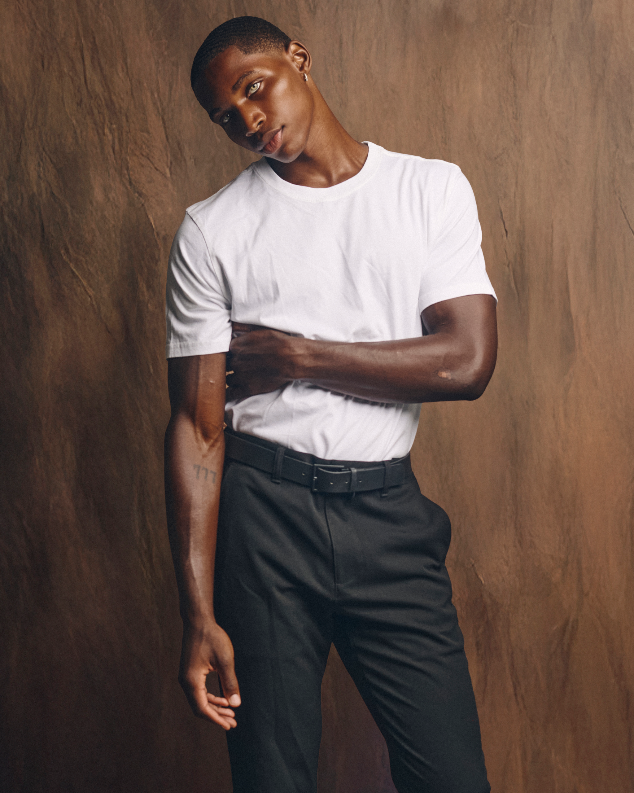 Model Devin Graham in a white T-shirt and black trousers against a brown backdrop